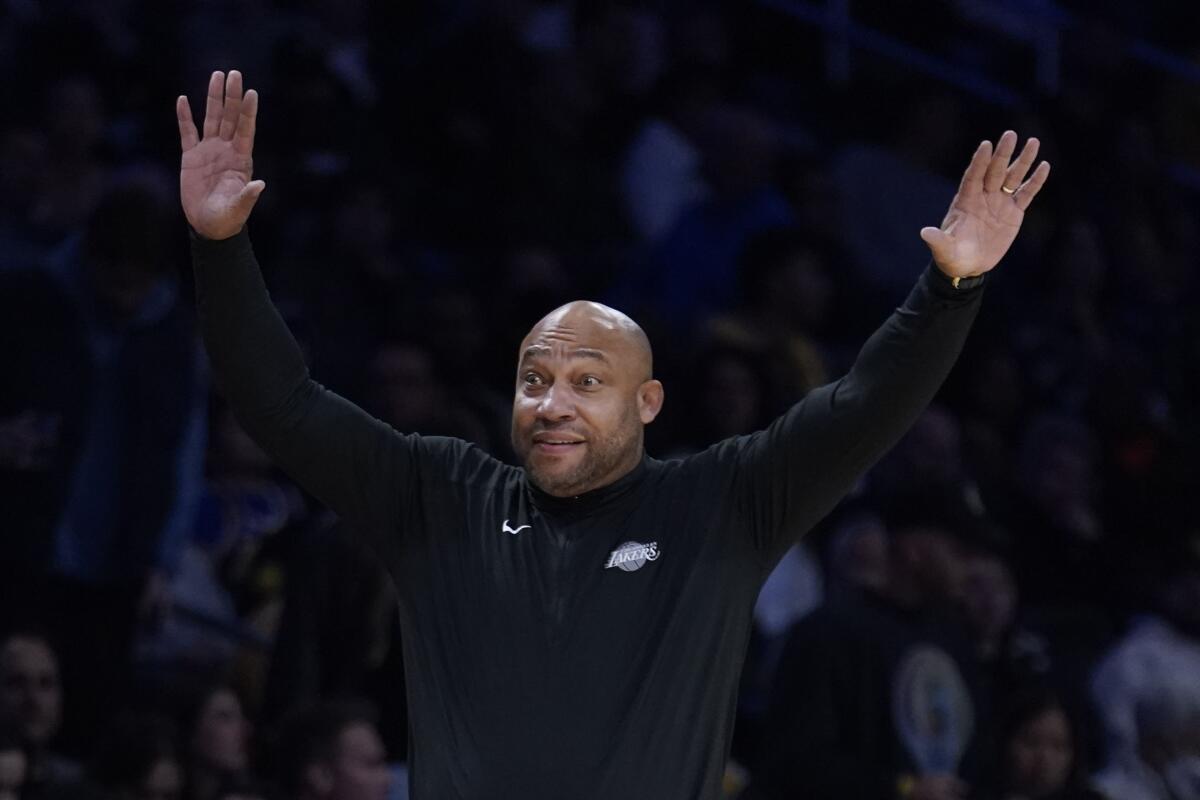 Coach Darvin Ham raises his arms overhead as he instructs Lakers players from the sideline.