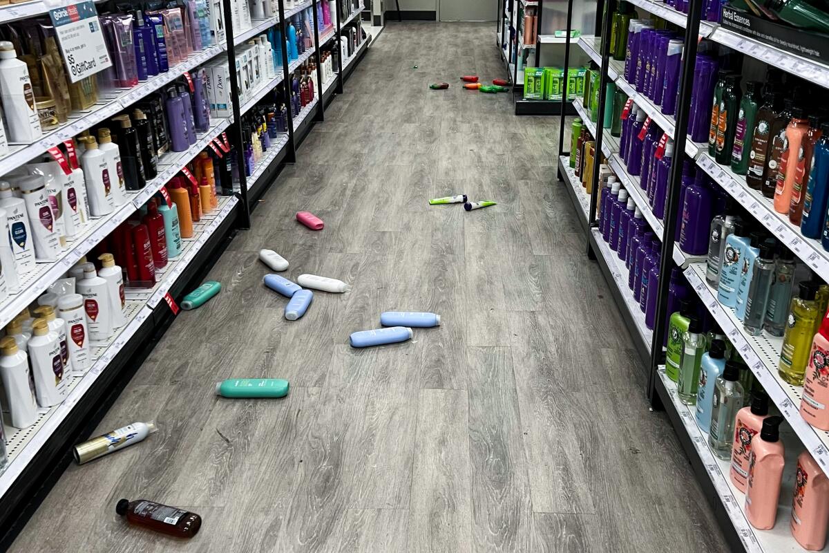 Bottles are on the floor of an aisle next of shelves of bottles.