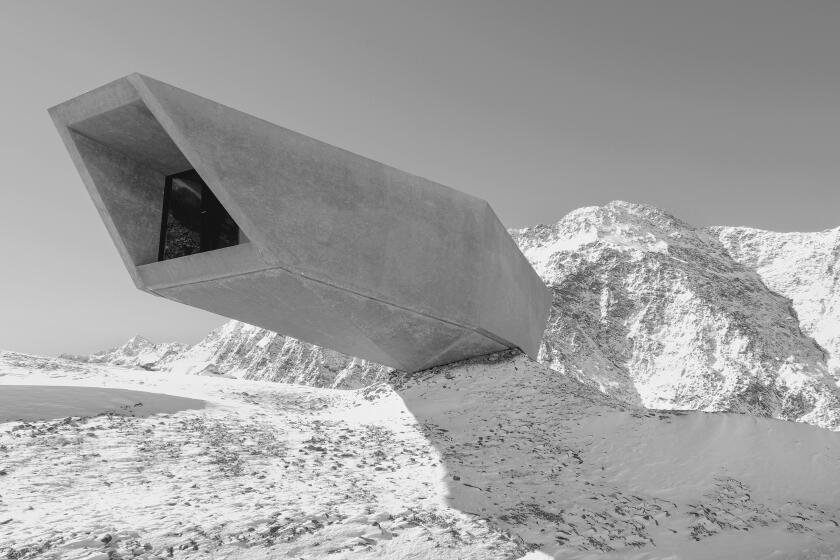 A long, rectangular concrete structure cantilevers out over thin air against the backdrop of snow-covered mountains.