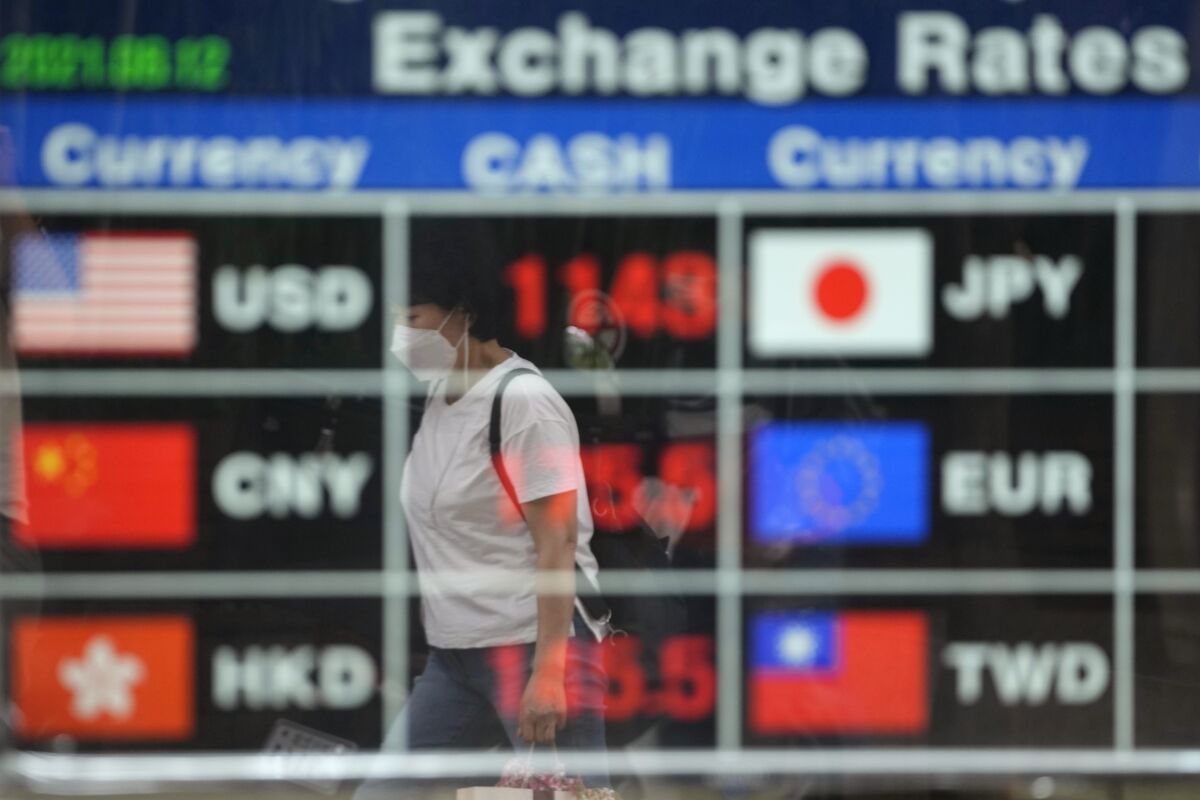 A woman wearing a face mask is reflected on an electronic foreign currency exchange rates in downtown Seoul, South Korea, Thursday, Aug. 12, 2021. Asian shares were mixed Thursday as caution set in among investors following another wobbly day of trading on Wall Street.(AP Photo/Lee Jin-man)