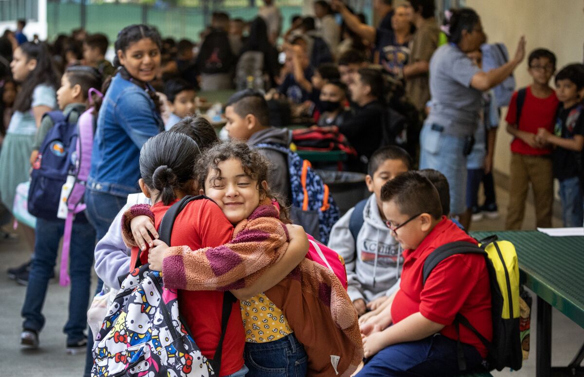 At the edge of a crowd, two girls hug.