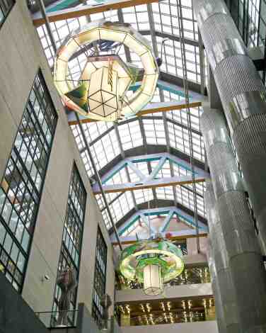 Looking up into a glass-roofed atrium with large hanging chandeliers