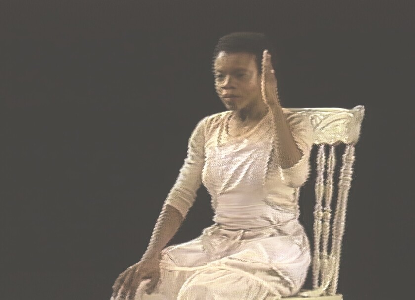 A woman sitting in a chair raises her arm in a still from "Chicken Soup," 1983.