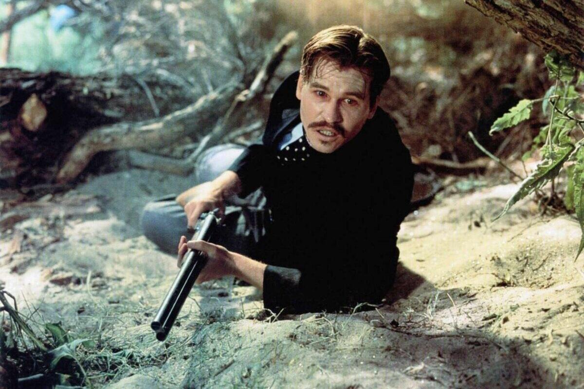 A man with a rifle takes cover in the underbrush.