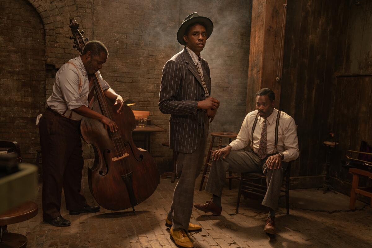 Chadwick Boseman, in period garb, stands in front of a man playing double bass.