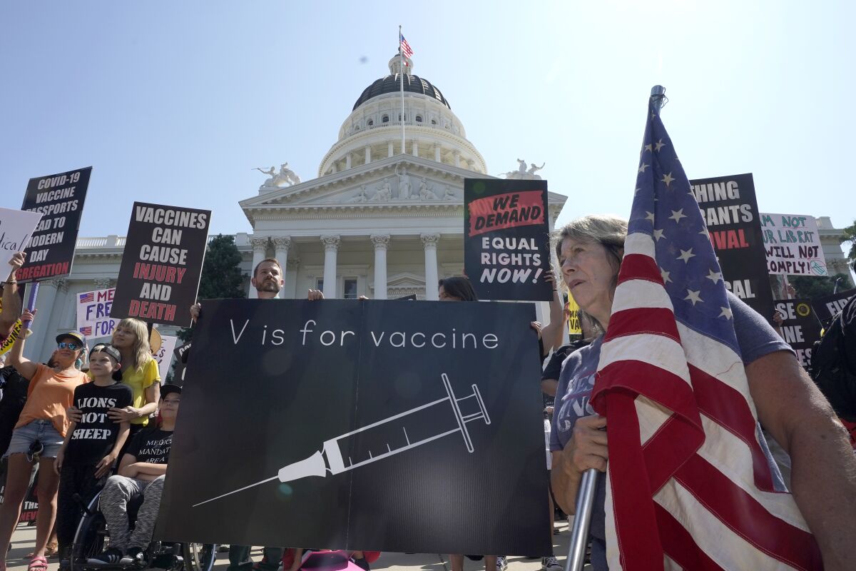 Protesters opposing vaccine mandates hold signs and a flag outside the Capitol in Sacramento