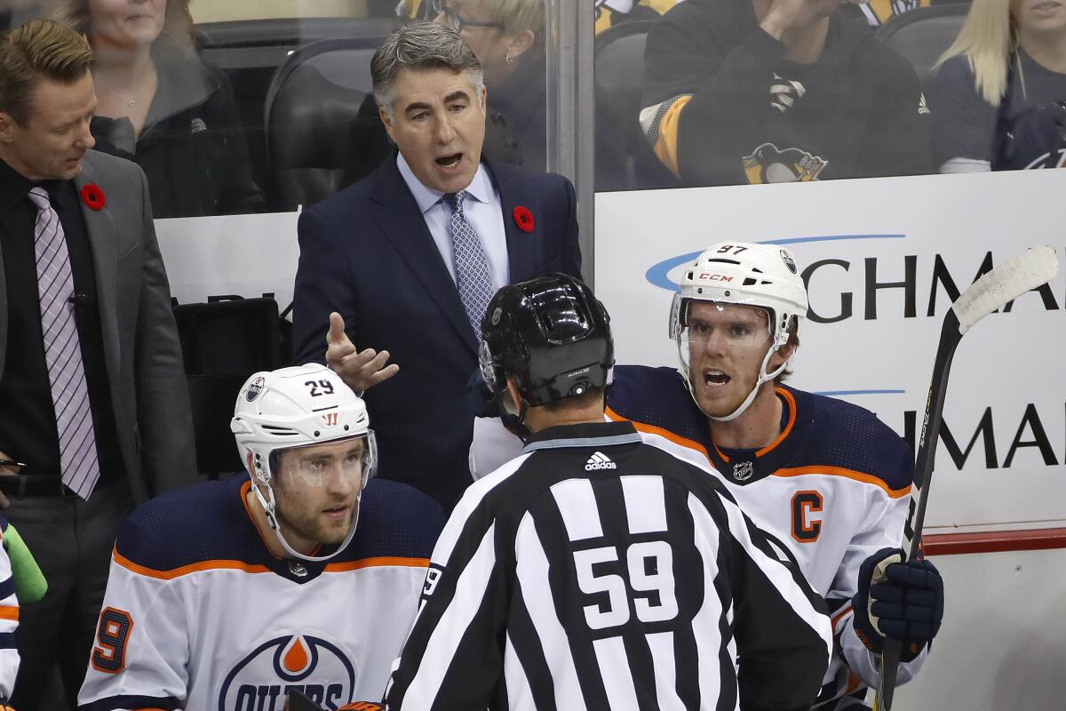 Oilers coach Dave Tippett stands behind Connor McDavid (97) and Leon Draisaitl (29) as he talks with linesman Steve Barton (59) during a game Nov. 2.