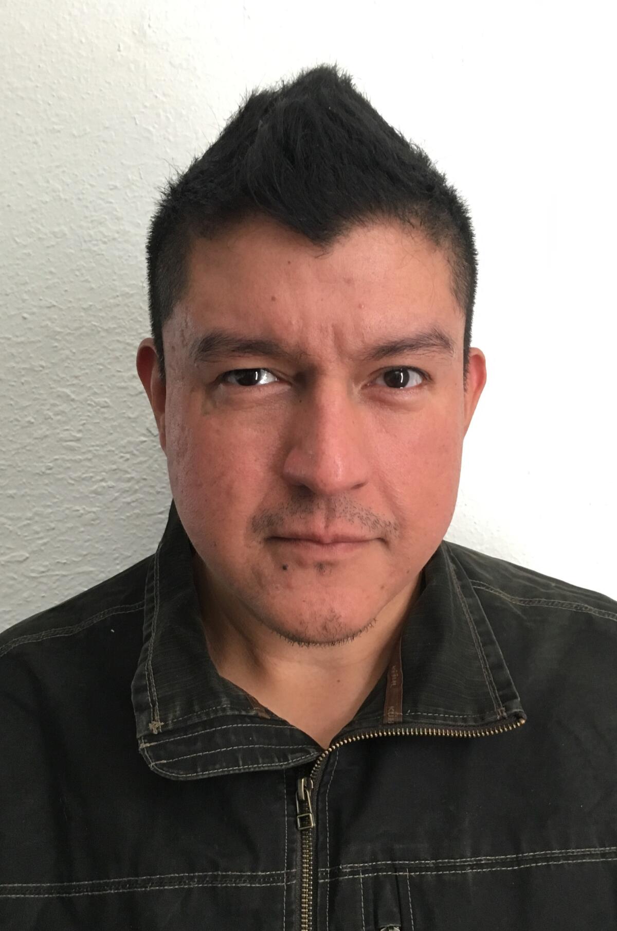 A portrait of a man with spiked black hair wearing a dark denim jacket.