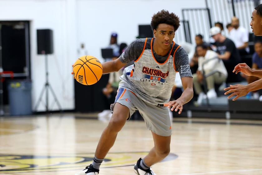 Alijah Arenas leans forward and dribbles the basketball on a court inside a gym.
