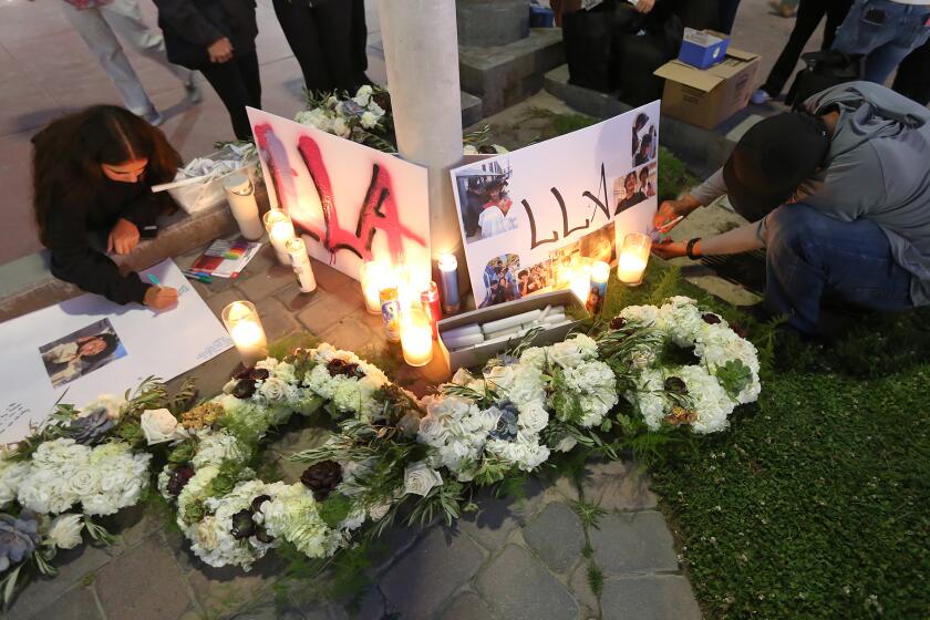 Friends write messages at a candlelight vigil shrine in honor of 15-year-old Aayan Randhawa, who went missing while swimming in the ocean off the shores of Huntington Beach on Sunday. The candlelight vigil, held at the Pier Plaza drew over a hundred family and friends who then walked to the end of the pier to throw flowers.