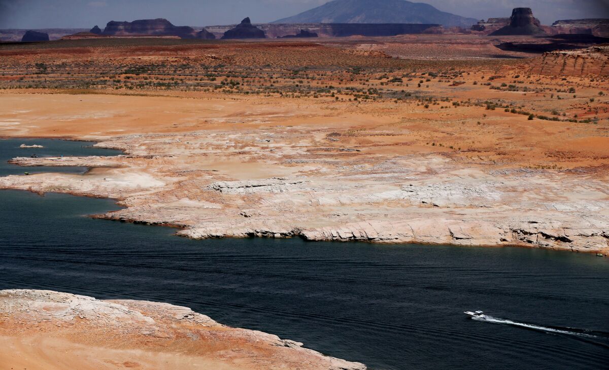 A speedboat seen from a distance on a body of water surrounded by red-hued land and mesas