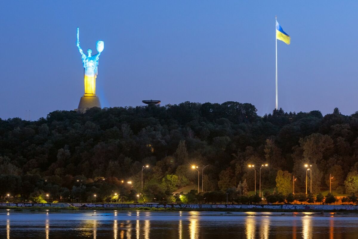The Motherland Monument, lighted in the colors of Ukraine's flag, stands above the Dnipro River in Kyiv.