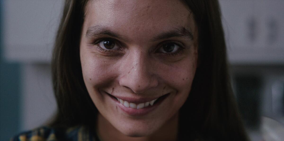 Close-up of a woman with an unnervingly broad grin and a scar