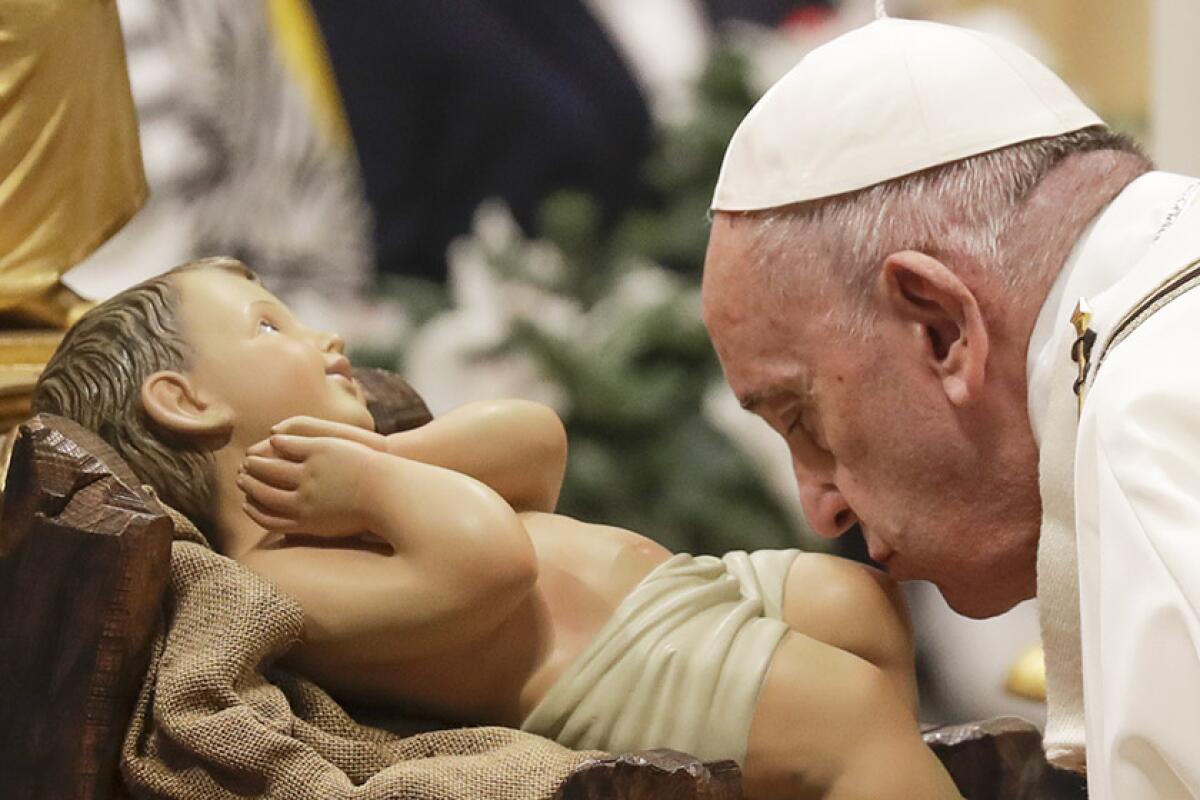 Pope Francis kisses a statue of baby Jesus as he celebrates Christmas Eve Mass in St. Peter's Basilica in Vatican City on Tuesday.