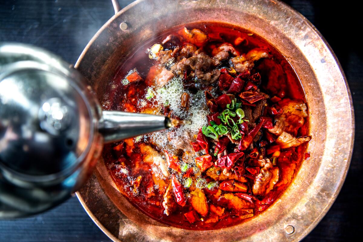 A tableside addition of boiling oil releases the fragrance of spices in water-boiled beef (called Kung fu boiled beef on the menu) at Xiang La Hui.