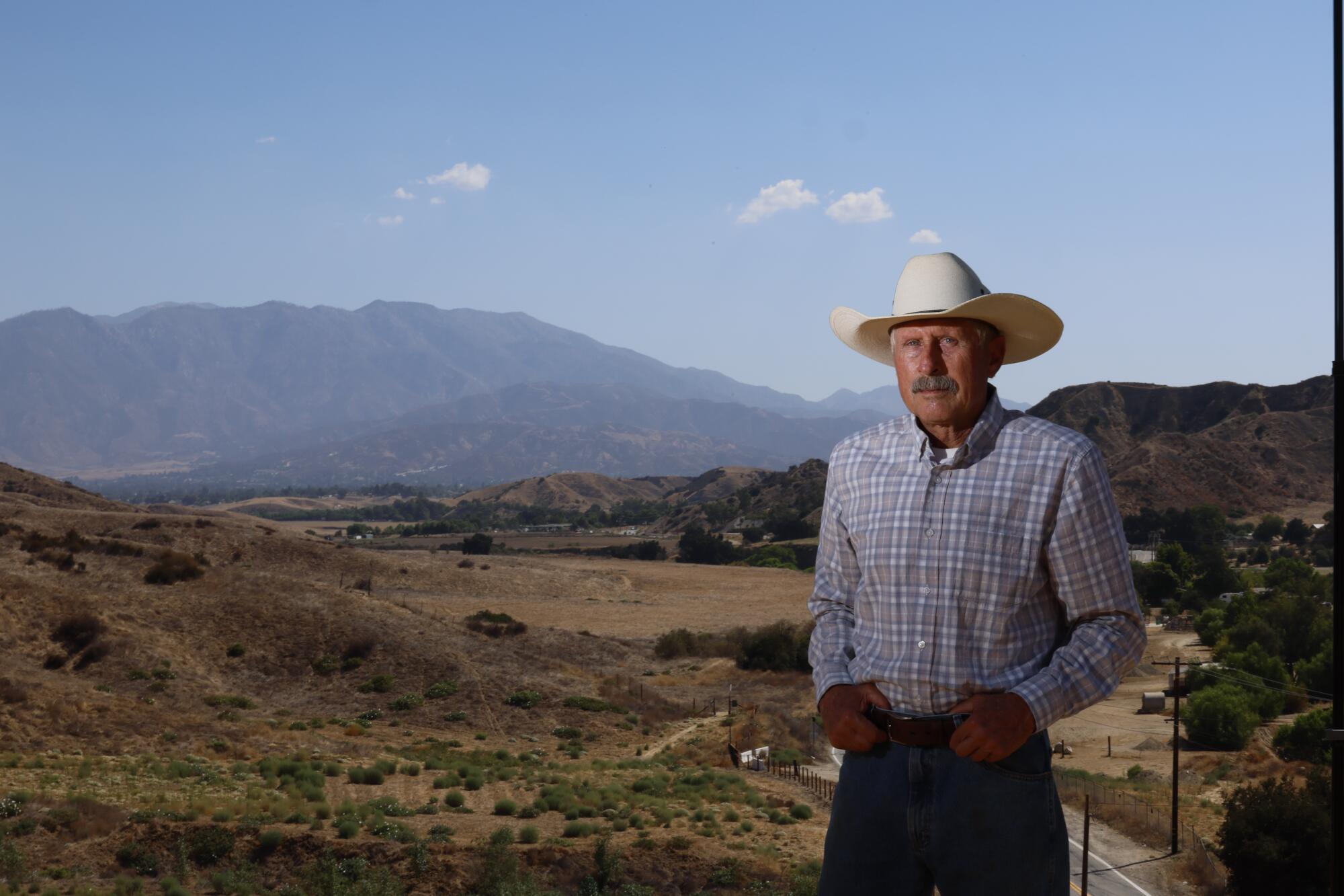 A man with a cowboy hat in front of mountains.