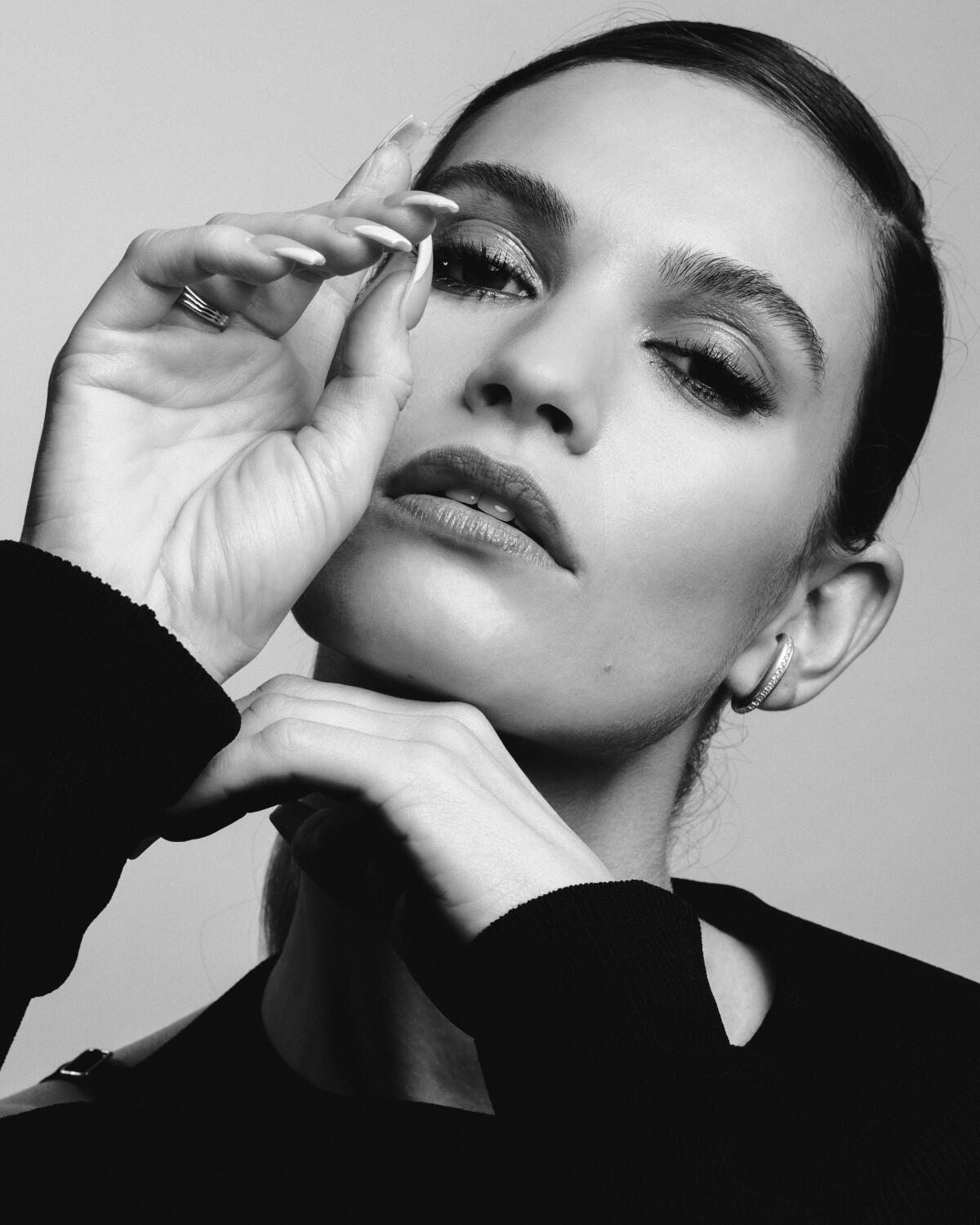 Lily James poses for a tight portrait with her hands near her face.