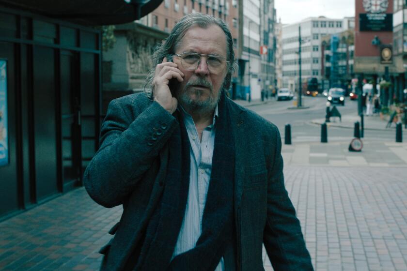 A bedraggled man stands on the sidewalk talking on a phone.