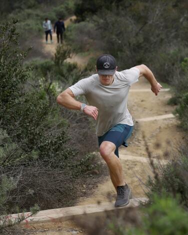 A man runs up a dirt trail among shrubs. 