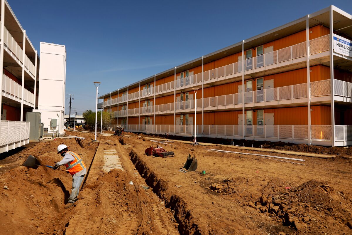 A worker digs a trench on the grounds between two brightly painted three-story towers made of shipping containers 