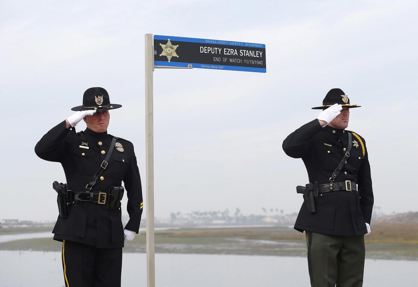 Gabe Ribbi, left, and Patrick Medeiros of the Orange County Sheriff's Department salute as a memorial sign is dedicated in honor of sheriff's Deputy Ezra Stanley on Monday near the Bolsa Chica wetlands in Huntington Beach. The ceremony was held 78 years to the day after Stanley was killed in a crash on Pacific Coast Highway while on duty in Huntington Beach.