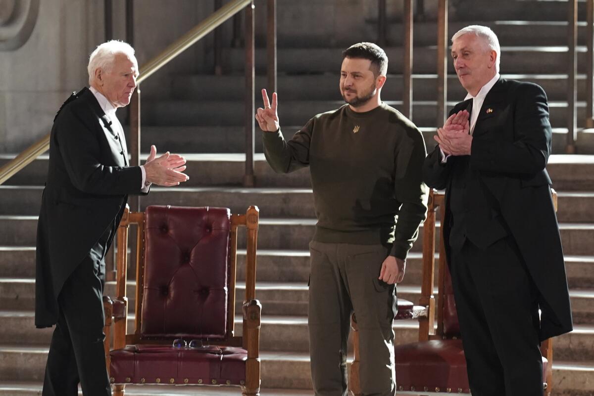 Ukrainian President Volodymyr Zelenskyy gives a peace sign as he is applauded by Speaker of the House of Commons, Sir Lindsay Hoyle, right, and Speaker of the House of Lords Lord McFall, left, following his address to parliamentarians in Westminster Hall, London, during his first visit to the UK since the Russian invasion of Ukraine.Wednesday Feb. 8, 2023. (Stefan Rousseau/pool photo via AP)