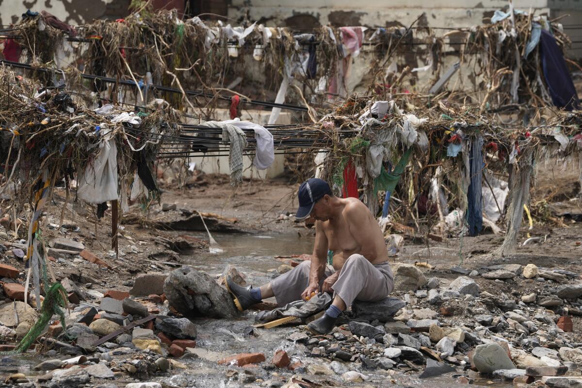 A man washes his clothes in a stream near debris left after flood waters devastated a village.