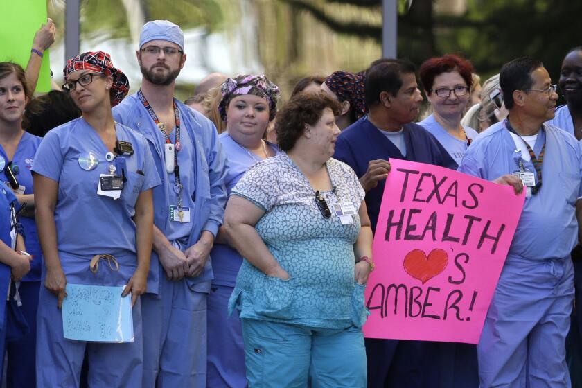 Workers at Texas Health Presbyterian Hospital in Dallas assemble Thursday. One holds a sign supporting nurse Amber Vinson, who contracted Ebola after treating a patient there.