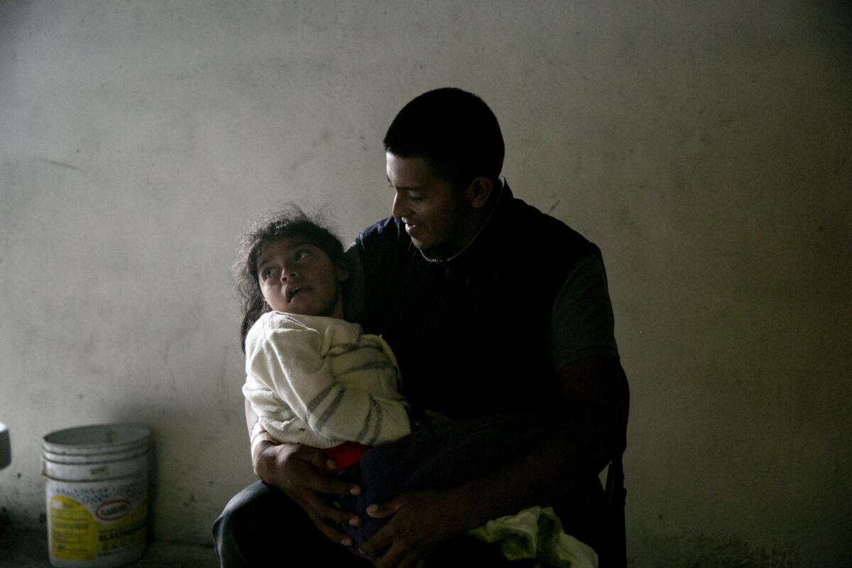 TIJUANA, MEXICO, November 30, 2018 | Juan Alberto Matthew cradles his 7-year-old daughter Lesly Alberto Matthew as they wait for Mark Lane of the Minority Humanitarian Foundation to hand them the right size diapers at a shelter for Central American migrants in Tijuana, Mexico. Lesly has cerebral palsy and hadn't received her medication since she was in Honduras. Lane pledged to connect her with the right supplies and services. | PHOTO/SAM HODGSON Staff photographer, San Diego Union-Tribune. ©2018