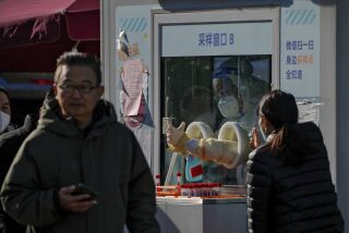 Un trabajador con ropa de protección desinfecta sus fuantes mientras la gente se hace pruebas rutinarias de COVID-19 en Beijing, China, el jueves 8 de diciembre de 2022. (AP Foto/Andy Wong)