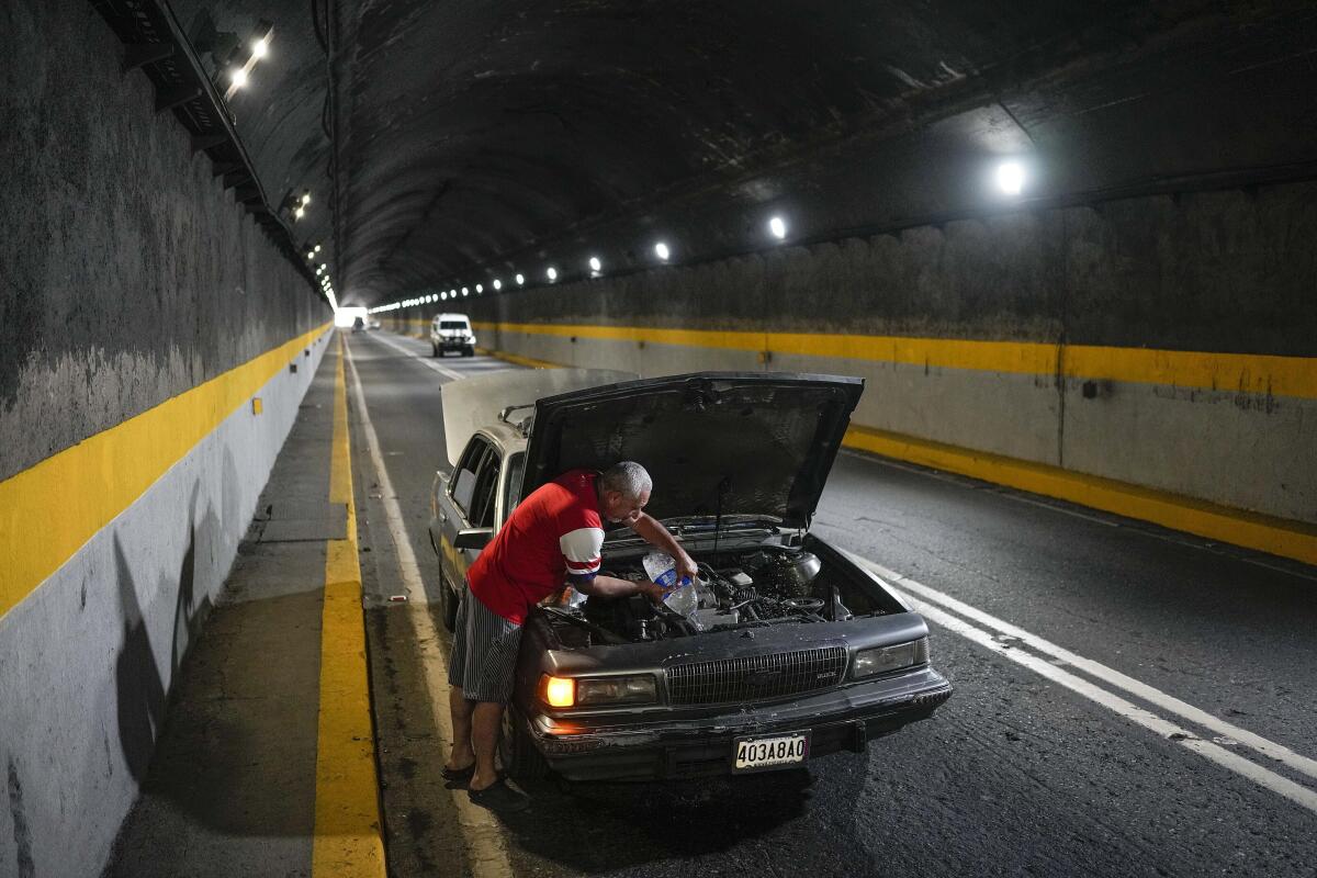 A man tries to cool down his overheating car by pouring water into the radiator in a road tunnel.