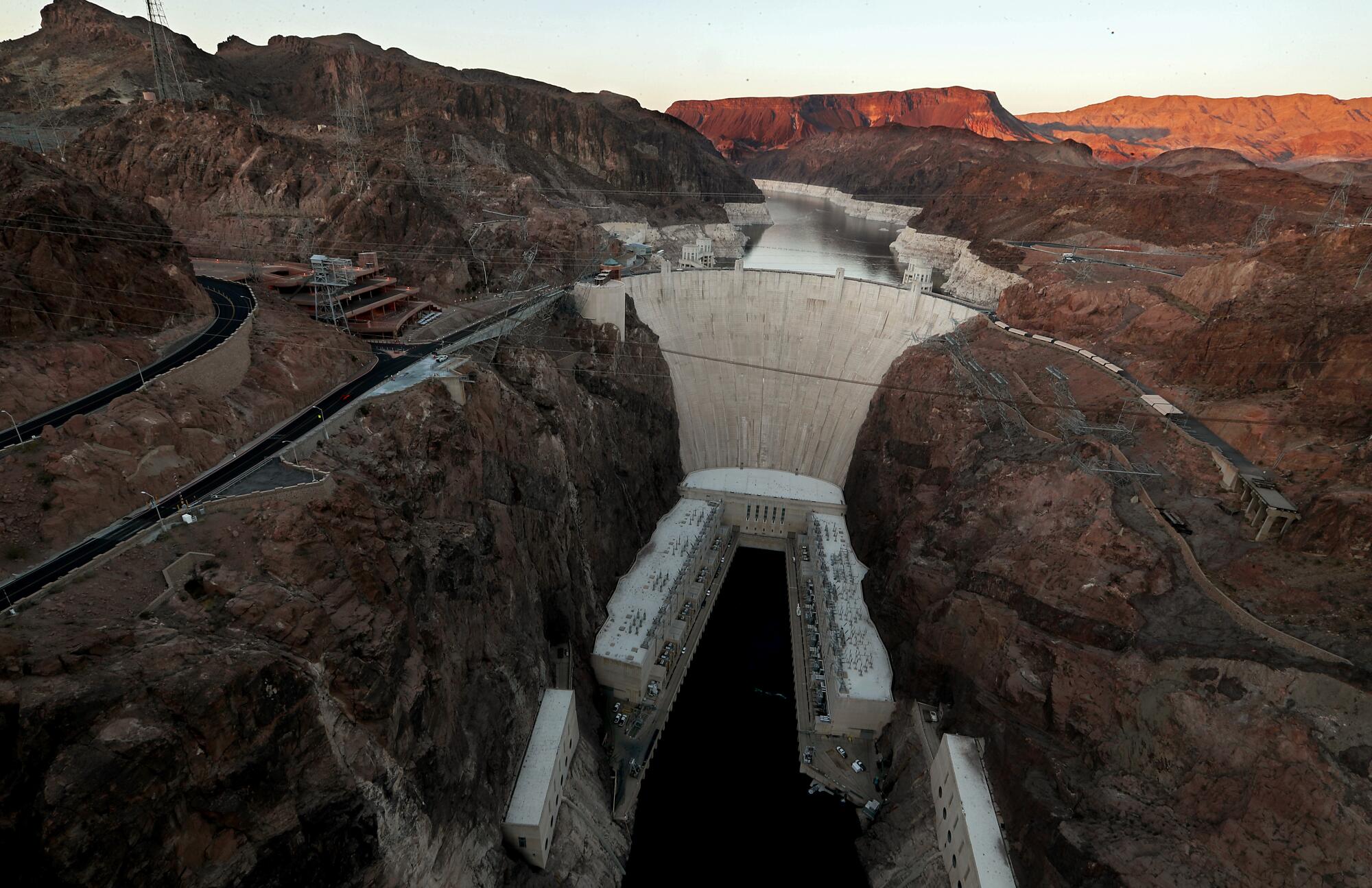 The Hoover Dam stands in front of Lake Mead, where white surfaces on the lake's rocky edges show how low water levels are.