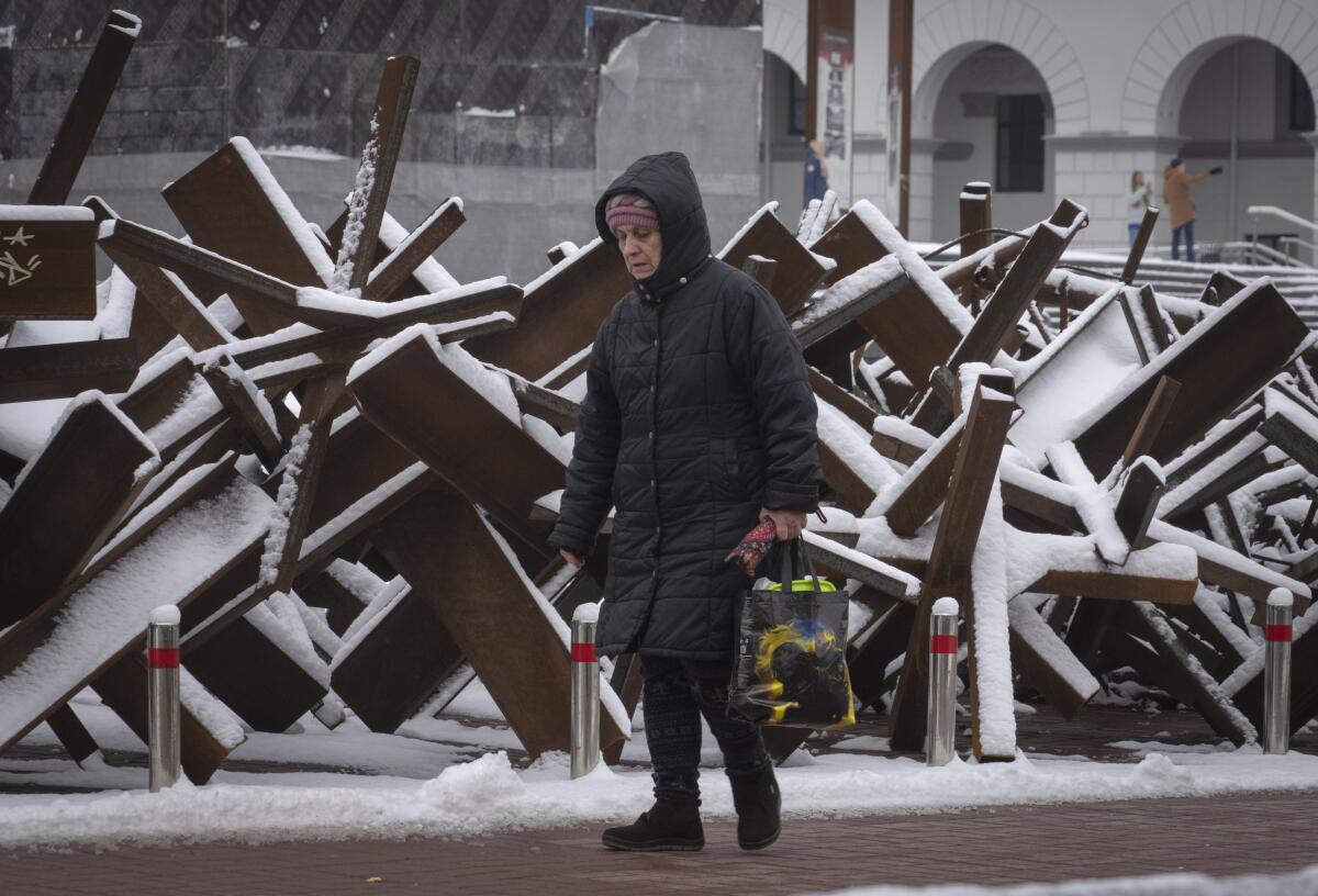 A woman walks by snow-covered metal angle beams piled to form a barrier 