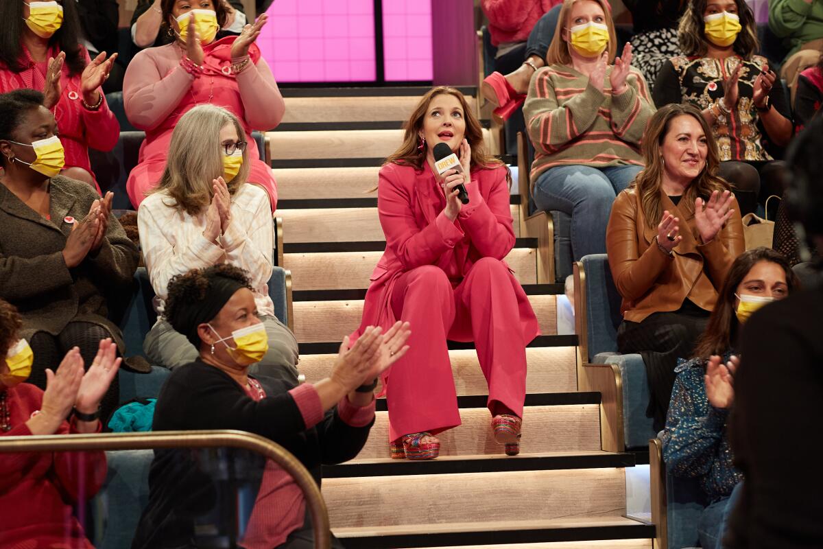 A woman in a fuchsia colored  suit sits with her audience along aisle stairs.