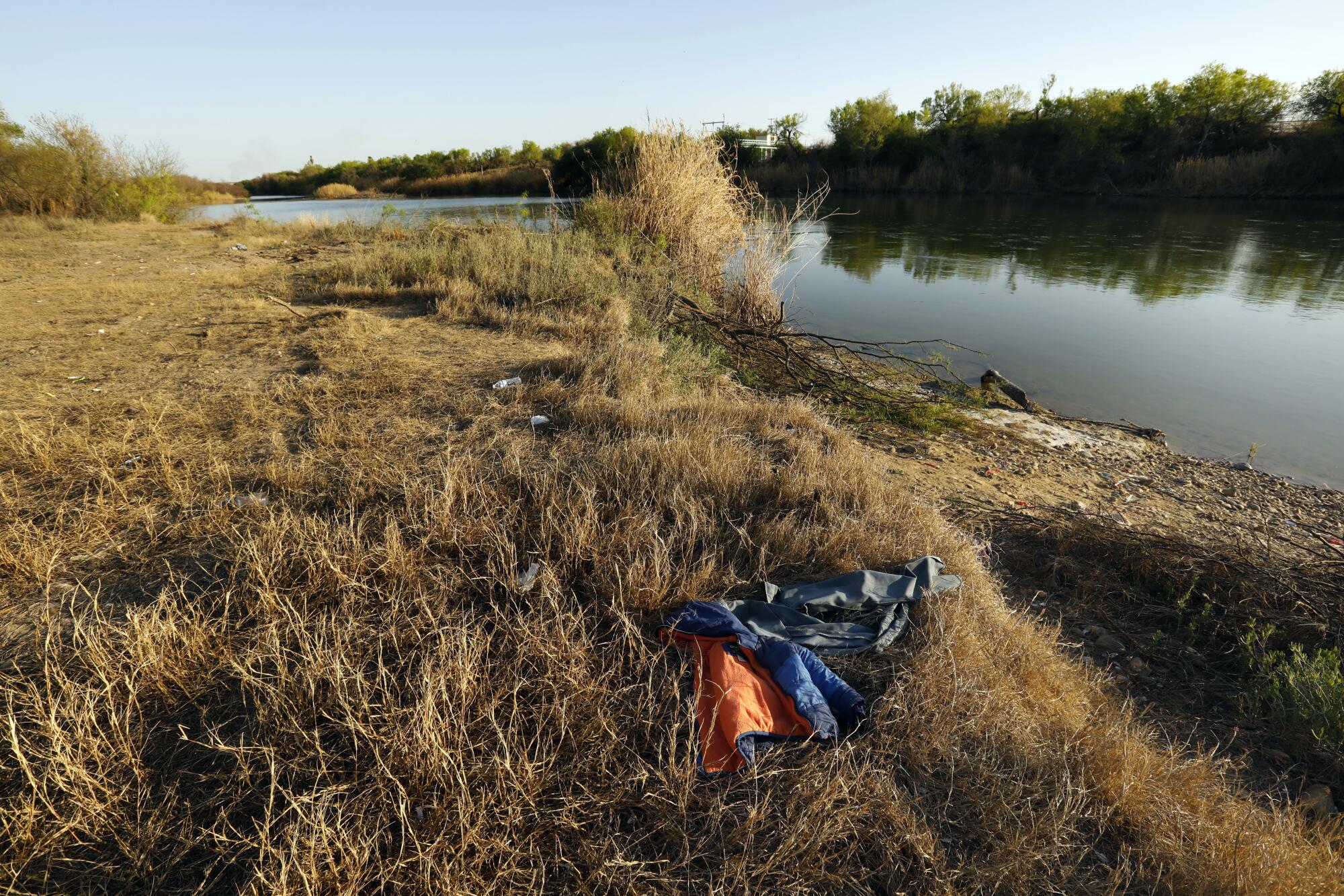 A child's jacket and pants in dry brush next to a riverbank