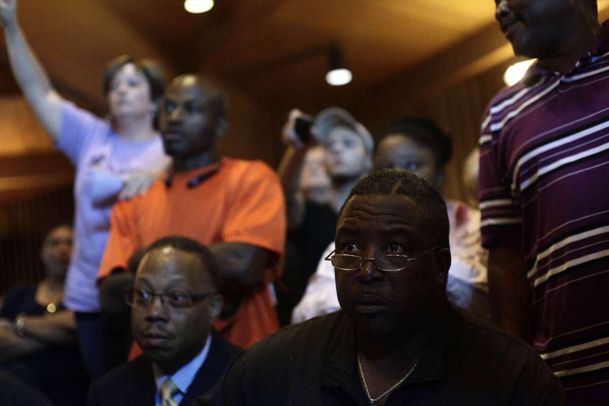 Ferguson residents and activists listen as Missouri Gov. Jay Nixon speaks during a news conference on the fatal police shooting of 18 year-old Michael Brown.