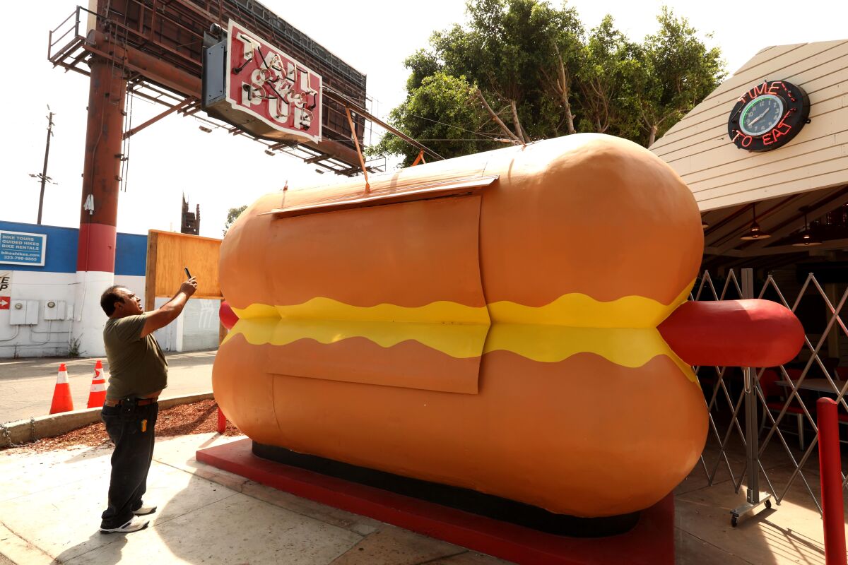 A man takes a picture of a stand shaped like a giant hot dog