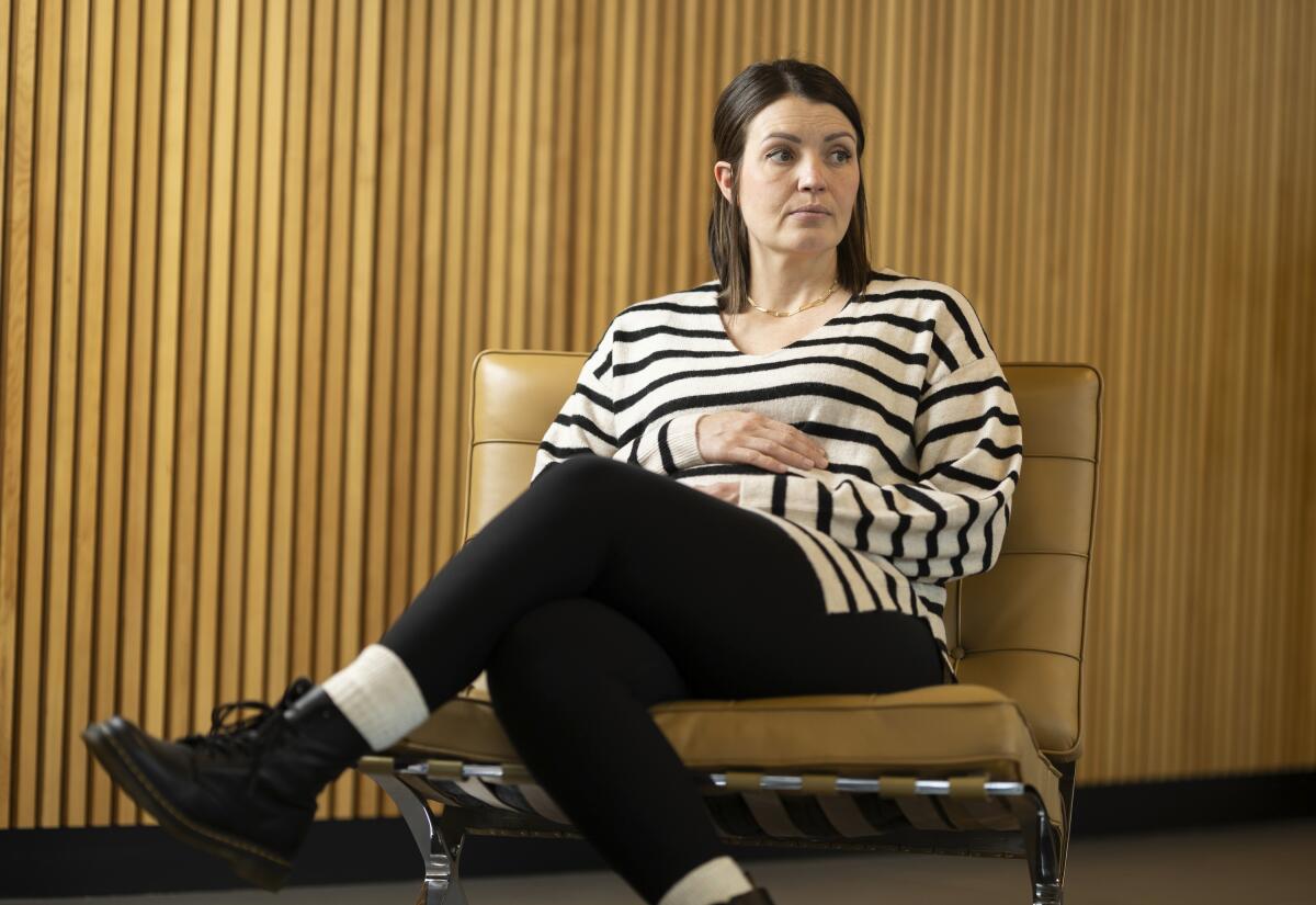 A woman sits with her arms over her stomach.