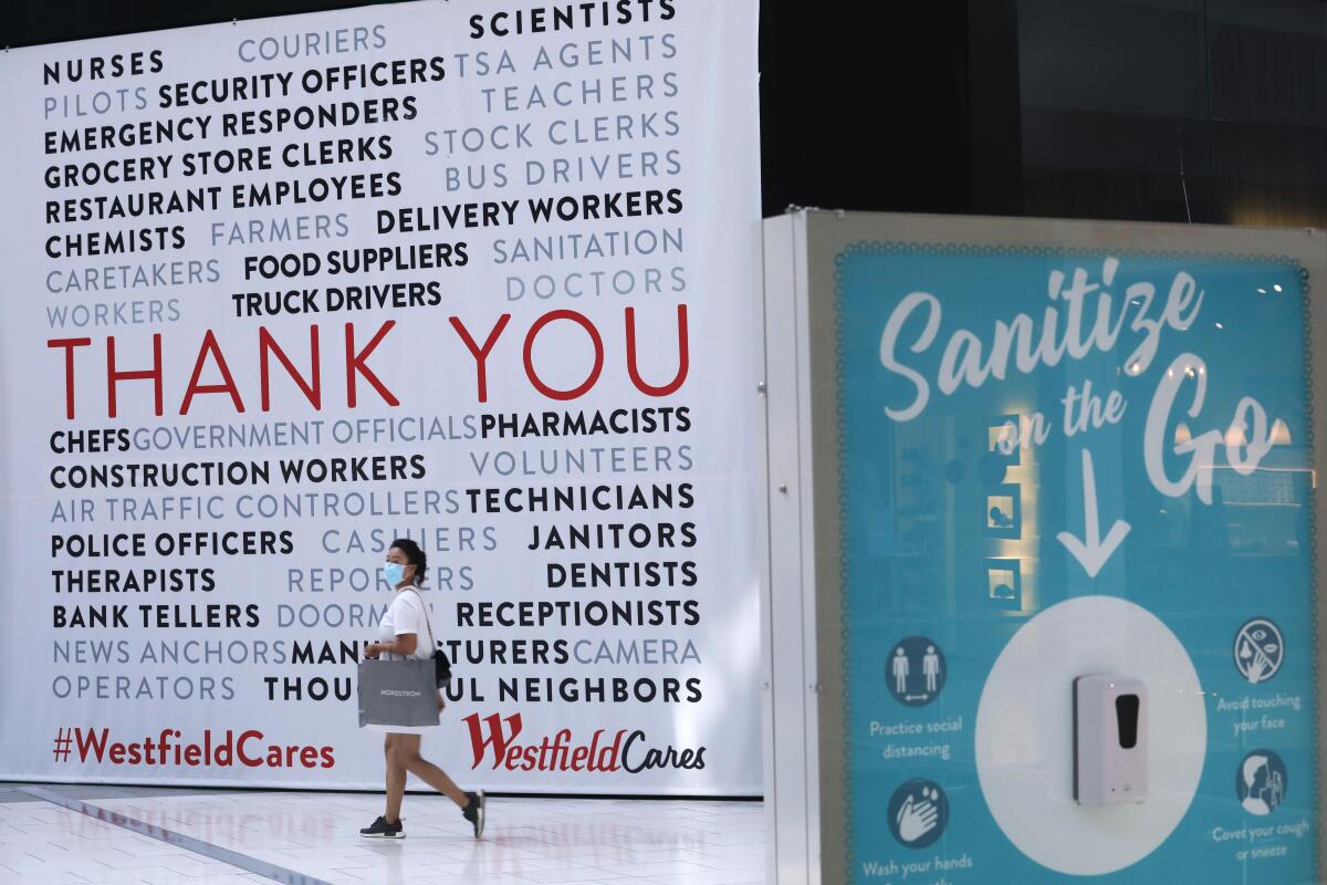 A person walks in front of a wall at a Westfield mall with messages thanking workers 