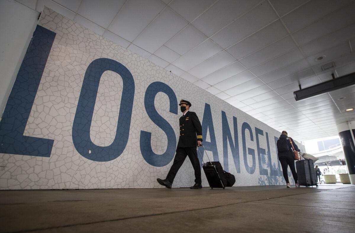 People with masks on rolling their luggage at LAX.