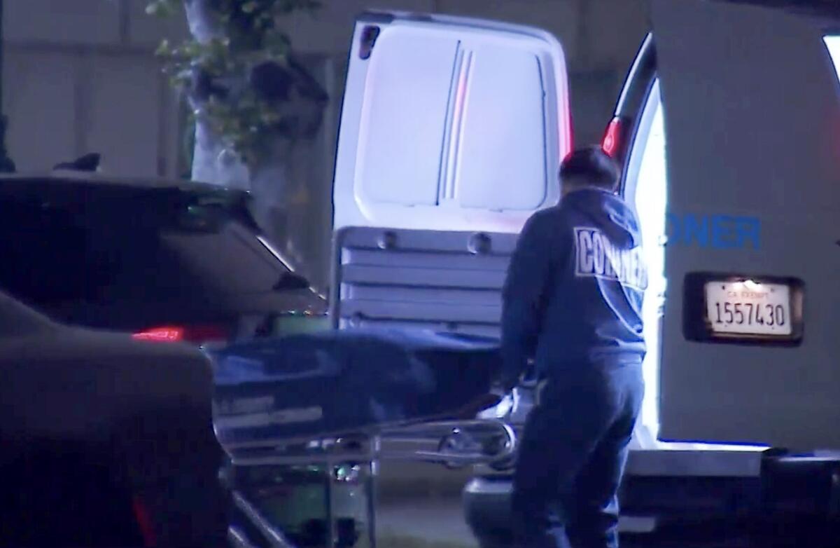 A stretcher is rolled to the open door of a coroner's van. 