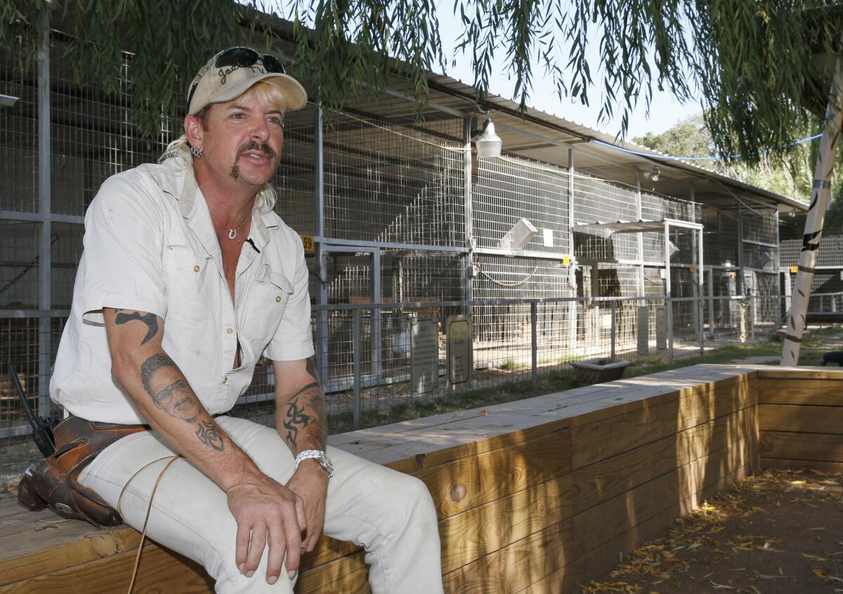 A man with a mustache and cap sits in front of animal cages