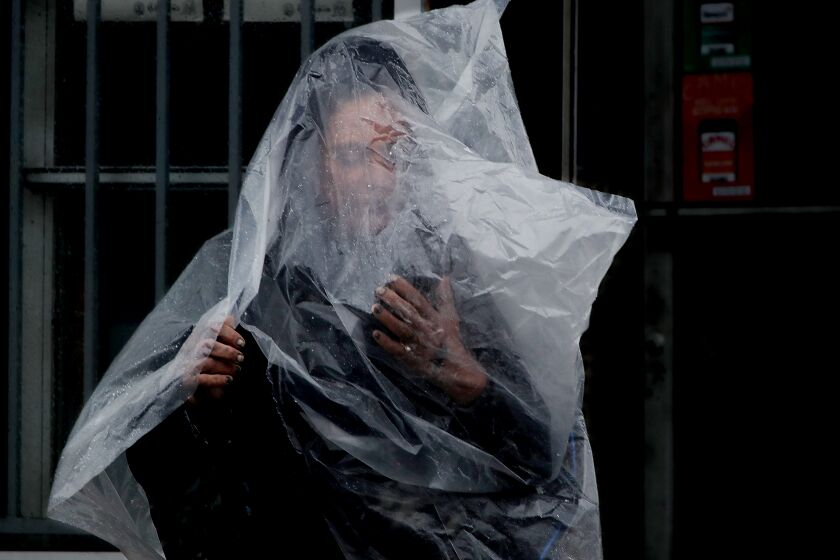 LONG BEACH, CALIF. - MAR. 28 ,2022. A woman uses a plastic sheet to shelter from a rainstorm in Long Beach on Monday, Mar. 28, 2022. (Luis Sinco / Los Angeles Times)