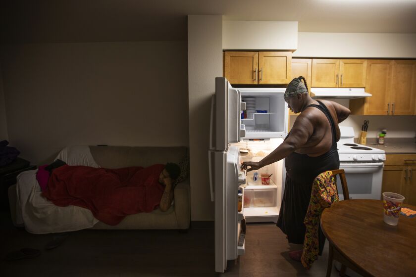 LOS ANGELES, CA December 6, 2018: Leneace Pope kn own as ÒNieceÓ right, stands looking into her refrigerator while her friends slept on her sofa in Los Angeles, CA December 6, 2018. She had been living on the street and August 6th she moved into her supportive housing unit. Her friends have moved in and are sleeping on her sofa. (*Editors Note: Contact photo editor Mary Cooney should you have any questions. Please do not use this image for other stories. This image is for a future project by writer Tom Curwen.) (Francine Orr/ Los Angeles Times)