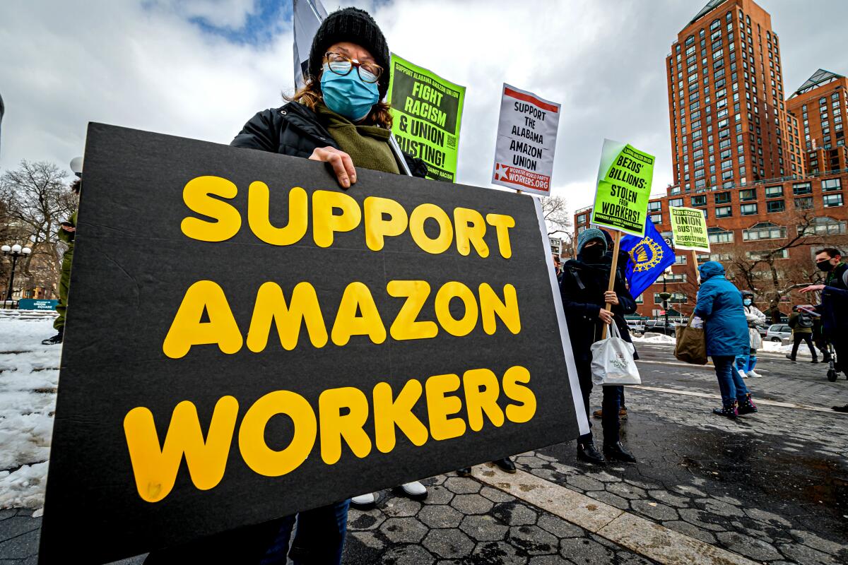 A woman in a mask alongside other labor activists holds a sign that says Support Amazon workers