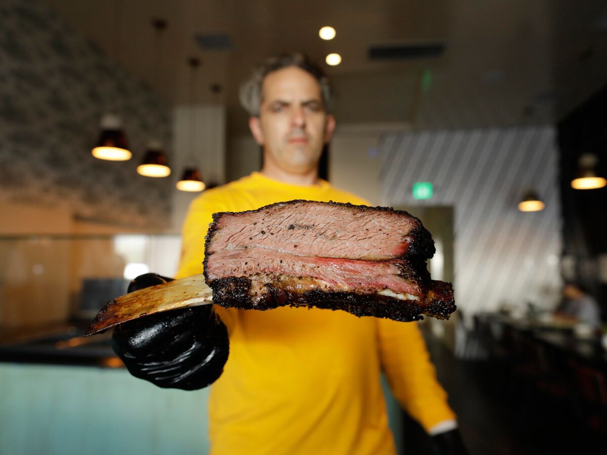 Burt Bakman holds a beef rib at Slab, his first restaurant. He is known for his Texas-style smoking at Trudy's Underground Barbecue, otherwise known as his San Fernando Valley backyard.