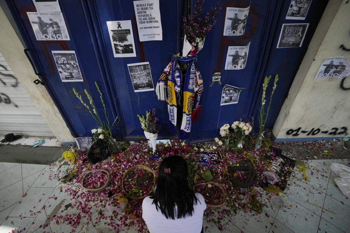 A woman takes a moment for the victims of Saturday's soccer match stampede in front of gate 13 at the Kanjuruhan Stadium in Malang, Indonesia, Tuesday, Oct. 4, 2022. Indonesian police said Tuesday that the gates at the soccer stadium where police fired tear gas and set off a deadly crush were too small and could only accommodate two at a time when hundreds were trying to escape. (AP Photo/Achmad Ibrahim)