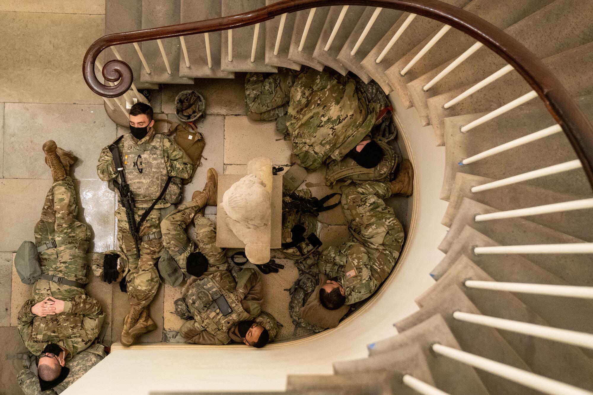 Service members in uniform sleep in an alcove below a curved stair