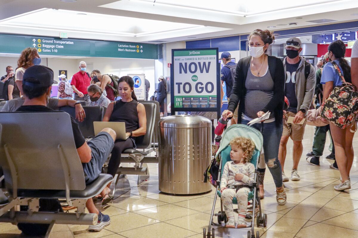 Passengers, some with and without masks, walk through the termial area at San Diego International Airport.