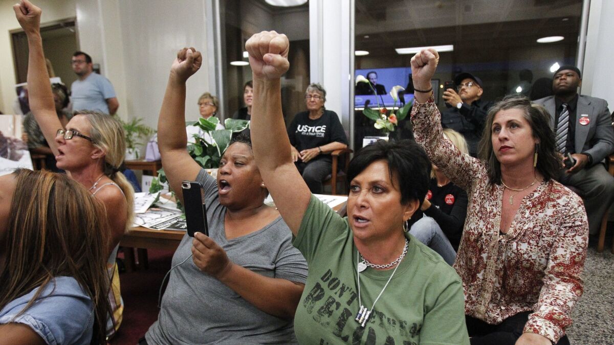 Amie Zamudio, left, Tasha Williamson, second from left, Maria Little, second from right, and Aaryn Belfer, right, raise their fists as they chant "Who killed Earl McNeil" while they watch a meeting on a television monitor outside of the council chambers Tuesday in National City.